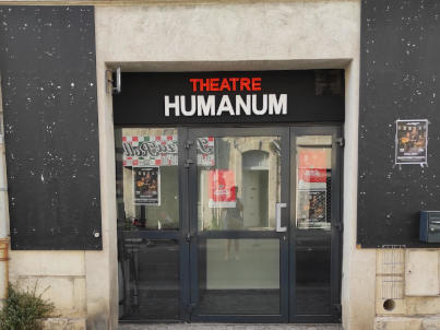 Photo de la façade du théâtre. Deux panneaux verticaux noir servant à mettre les affiches des spectacles encadrent l’entrée du théâtre. La porte est vitrée, et le nom du théâtre apparaît en couleurs au-dessus.