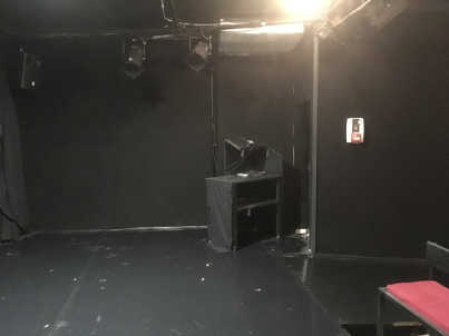 Photo de la scène sur laquelle un meuble vide sur roue est disposé. Il s’agit de la régie qui ce situe contre l'avant de la scène, à droite des gradins. On voit aussi des projecteurs et une enceinte suspendus au grill.